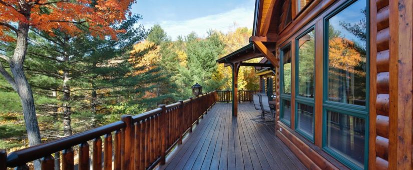 Cozy log cabin with a porch, surrounded by vibrant autumn foliage, showcasing sustainable timber frame design.